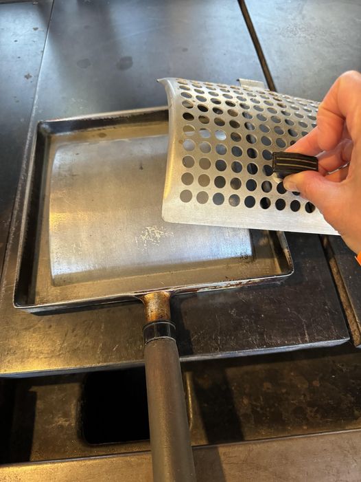 A 6-inch square kitchen implement, made from metal with a possibly bone handle, was located on a stove in an early 1900s American home.